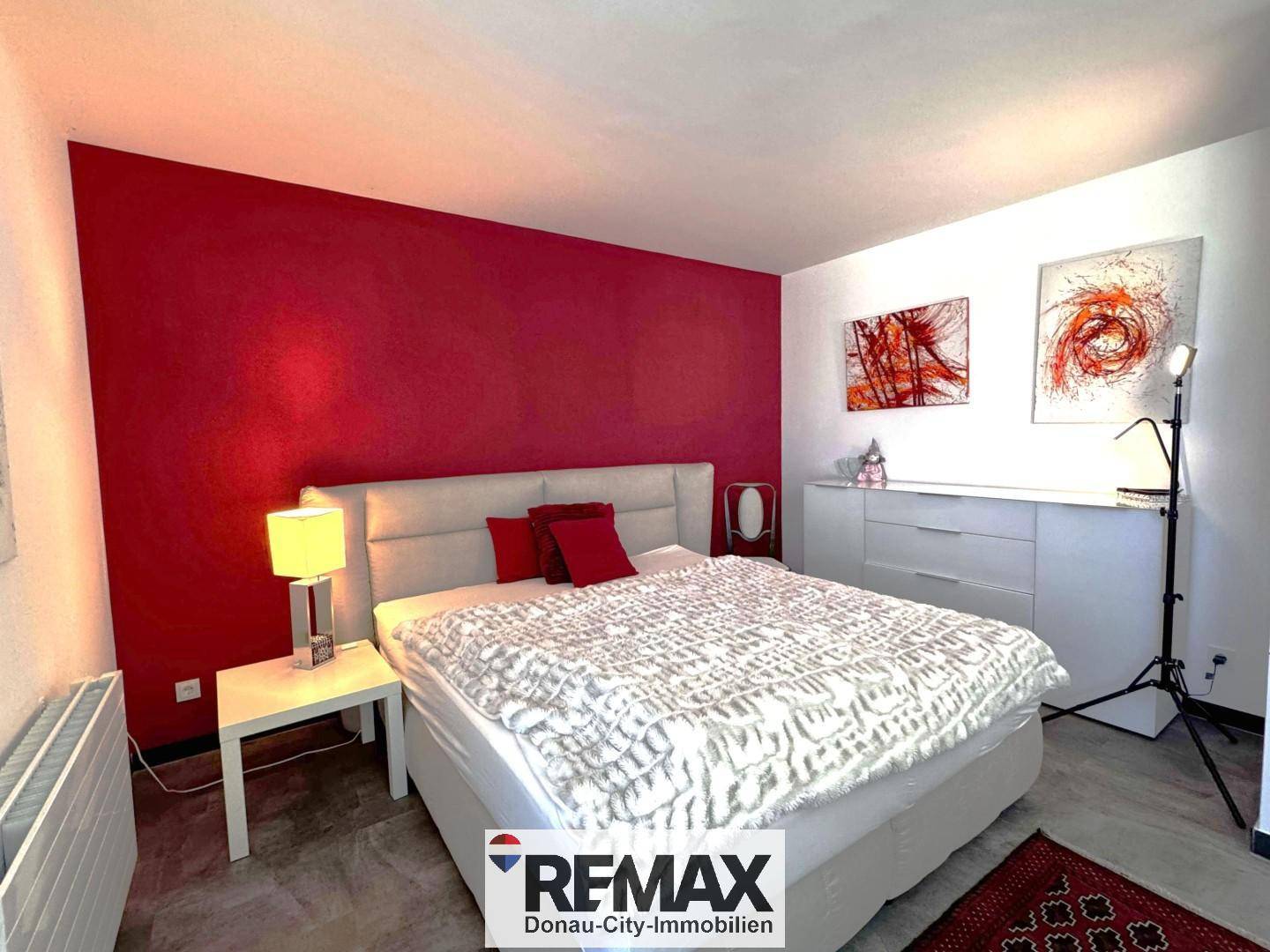 Geräumiges Schlafzimmer mit großem Bett, roter Akzentwand und moderner Dekoration.
