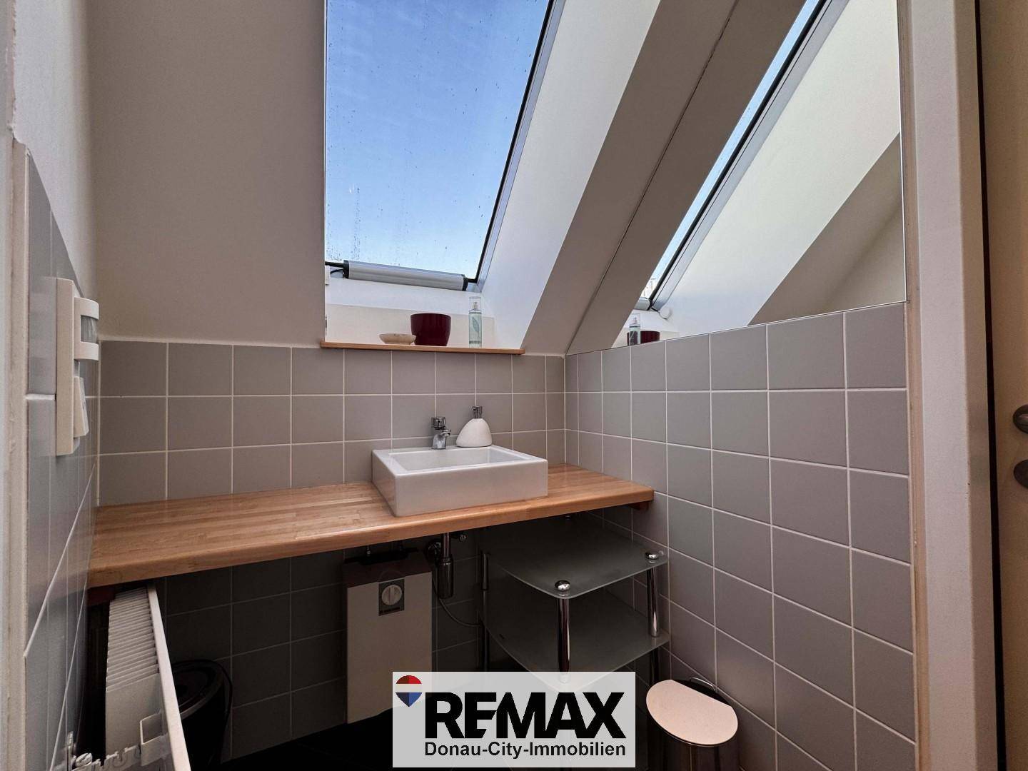 Kleines WC mit Waschbecken, Holzplatte und Dachfenster für natürliches Licht.