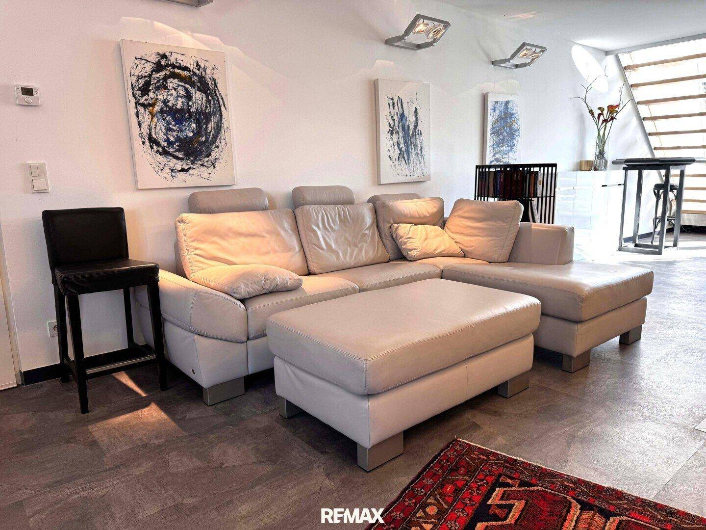Helles Wohnzimmer mit großem Ecksofa, modernem Kunstdekor und dunklem Bodenbelag.