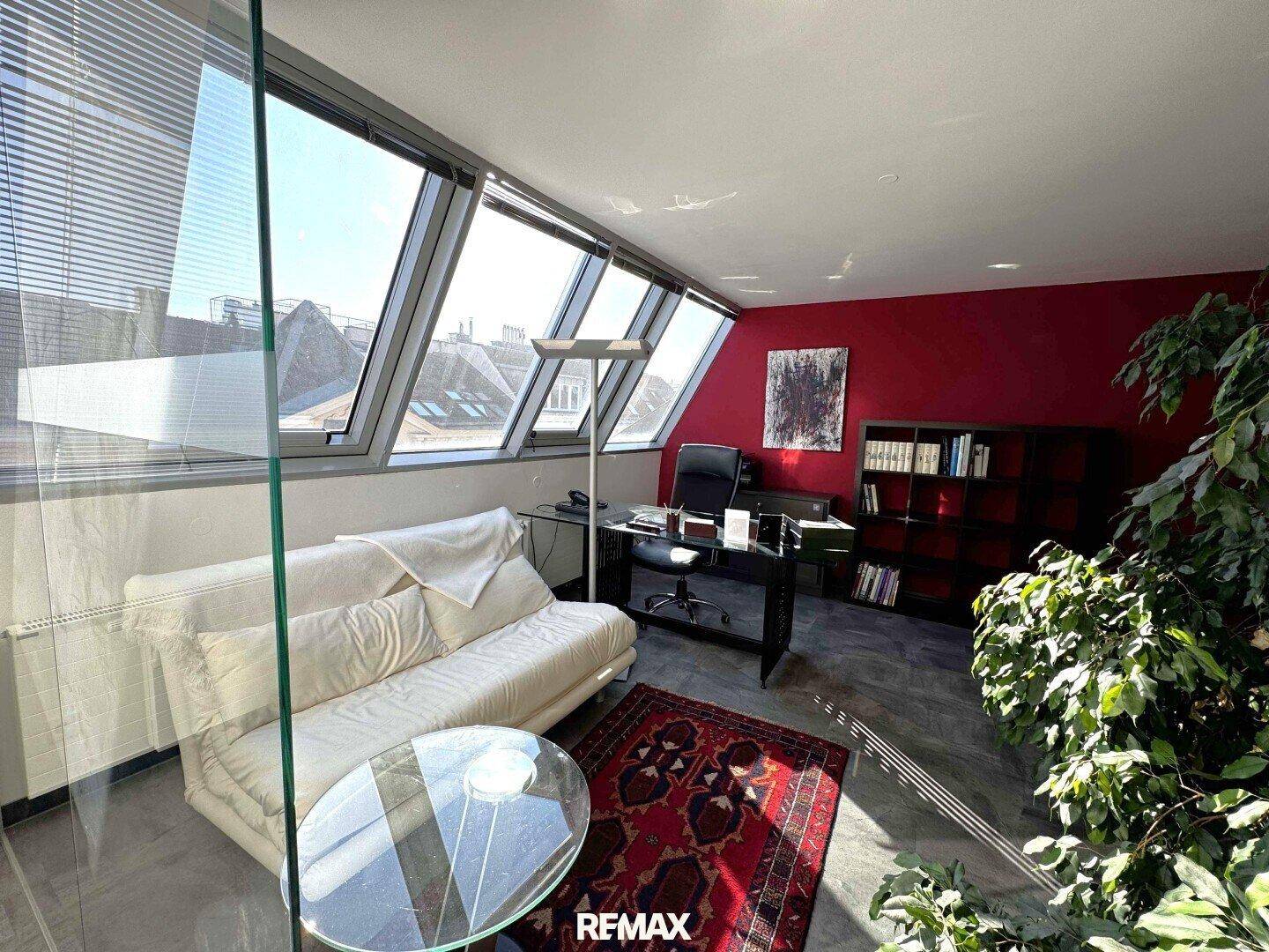 Modernes Büro mit gemütlichem Sofa, Glas-Couchtisch und schrägen Dachfenstern für helle Atmosphäre.