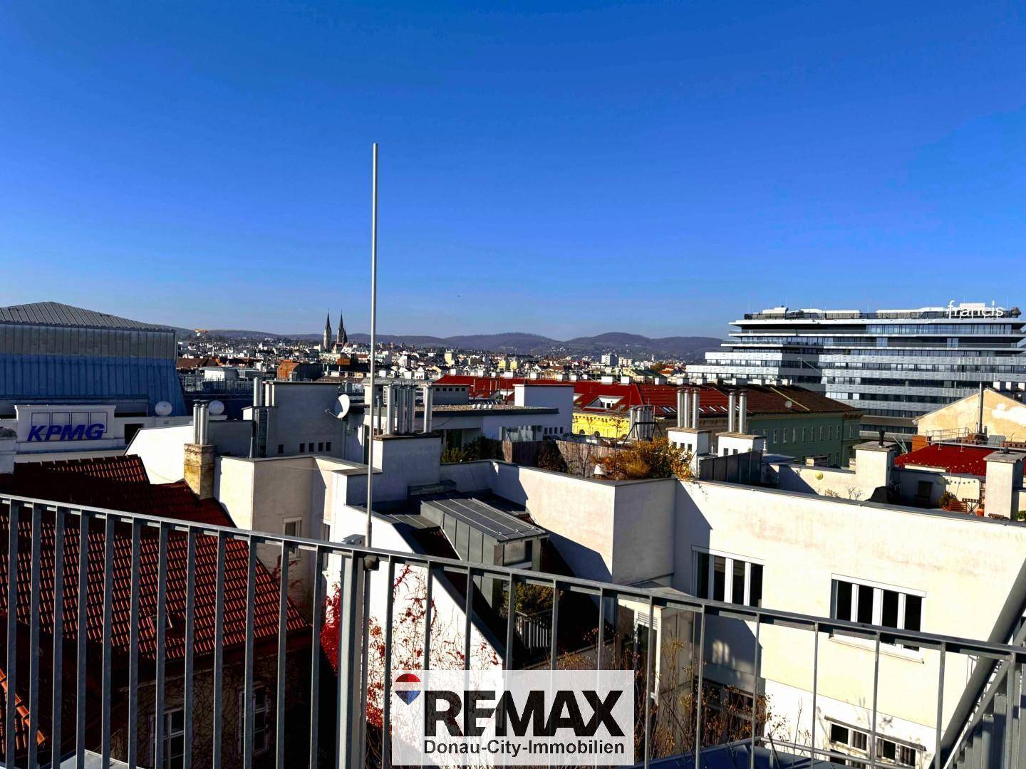 Dachterrasse mit Metallgeländer und Panoramablick auf die umliegenden Gebäude und die Stadt.