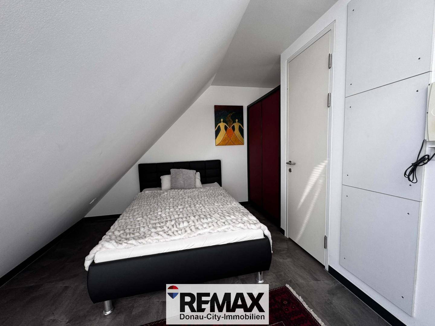 Schlafzimmer mit Einzelbett, Dachschräge und roter Akzentwand im Dachgeschoss.