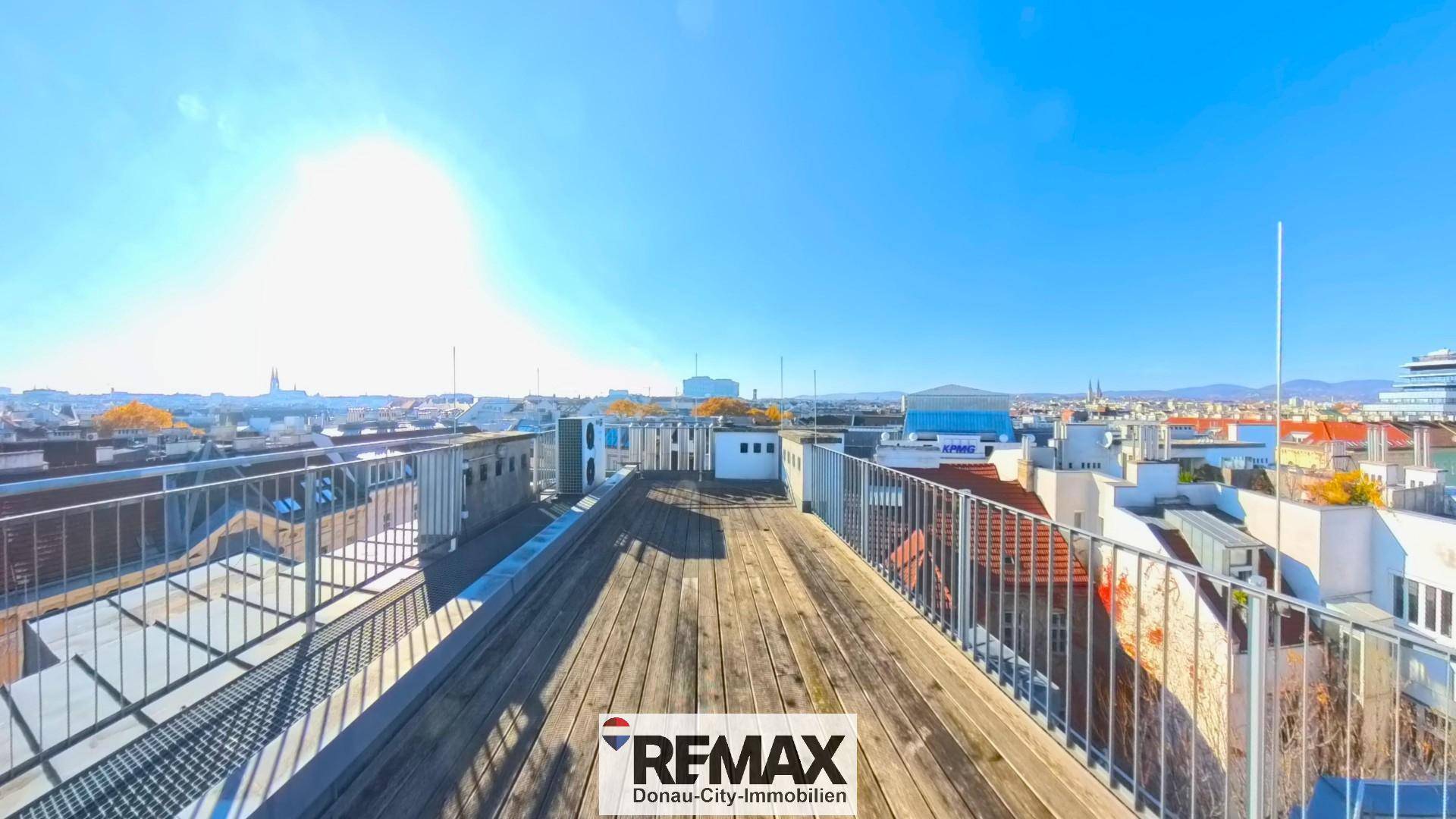 Sonnige Dachterrasse mit Holzbelag und Metallgeländer, bietet einen weiten Blick über die Stadt.