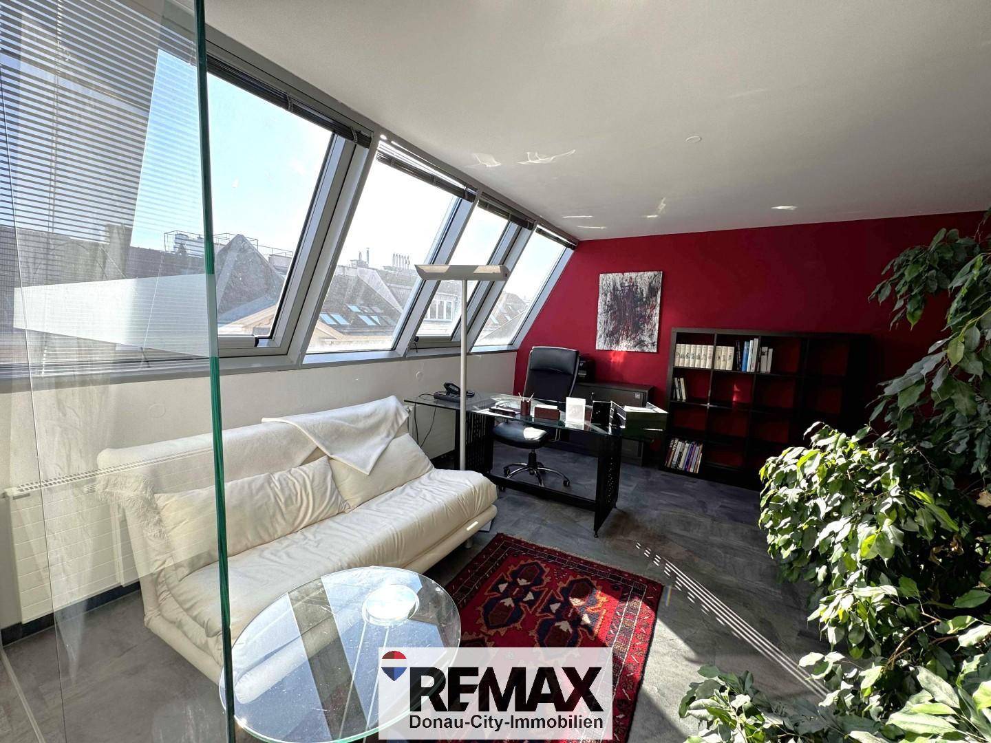 Modernes Büro mit bequemer Couch, Schreibtisch und großen Dachfenstern für viel Tageslicht.