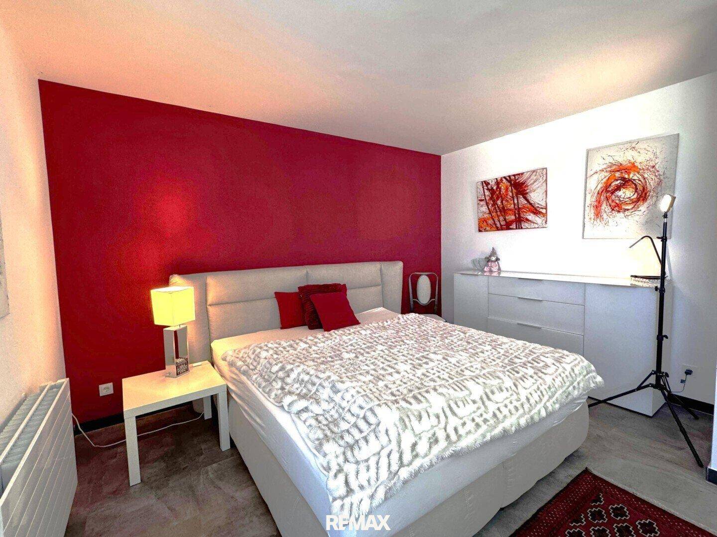 Hauptschlafzimmer mit Doppelbett, roter Akzentwand, weißer Kommode und moderner Kunst.