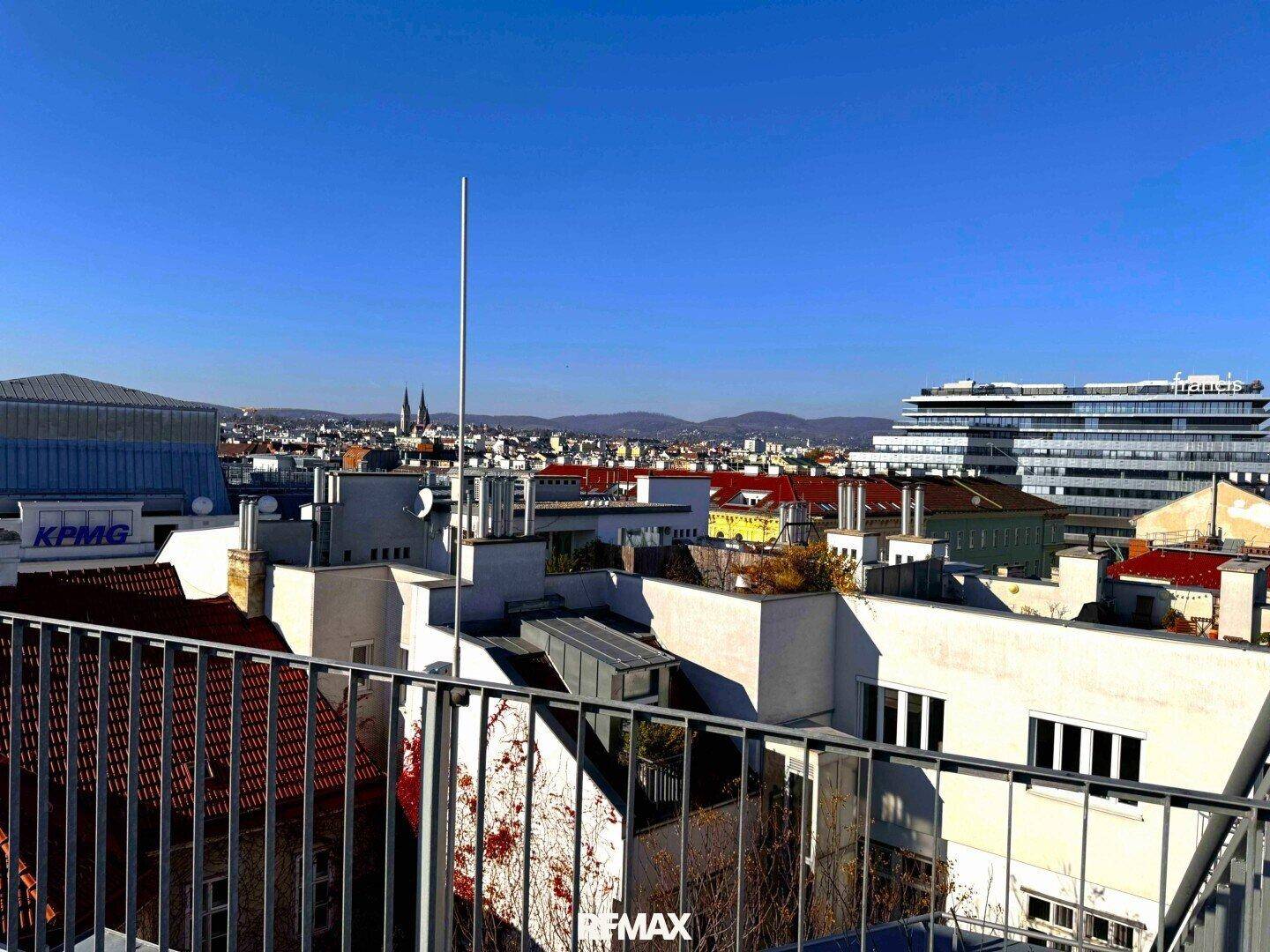Weitläufiger Stadtblick von einer Dachterrasse mit modernen Gebäuden und klarem Himmel.