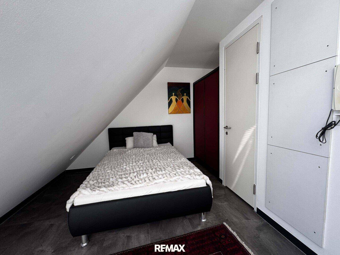 Schlafzimmer mit Einzelbett, Dachschräge und einem roten Kleiderschrank an der Wand.