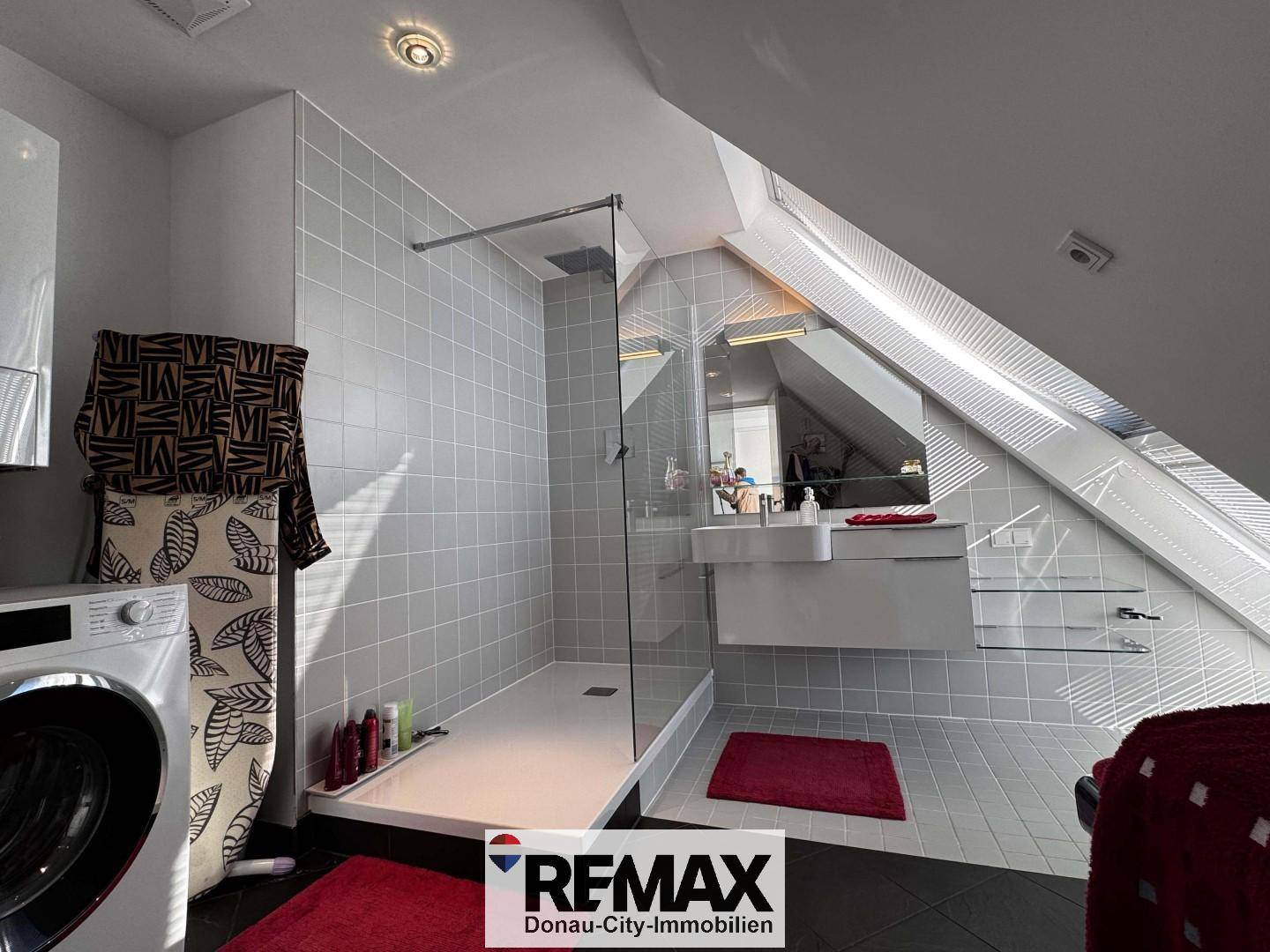 Helles Badezimmer mit großer begehbarer Dusche, modernem Waschtisch und viel Tageslicht durch Dachfenster.