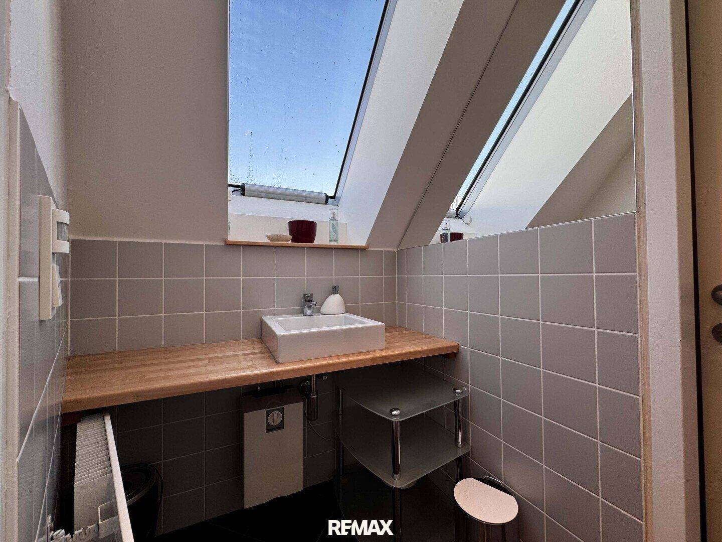Kleines Badezimmer mit Waschbecken, Holzplatte und einem Dachfenster für natürliches Licht.