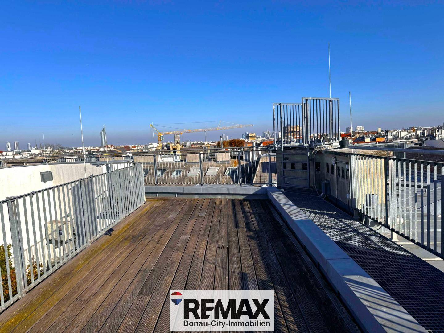 Geräumige Dachterrasse mit Holzboden und Metallgeländer, ideal für Entspannung mit Stadtblick.