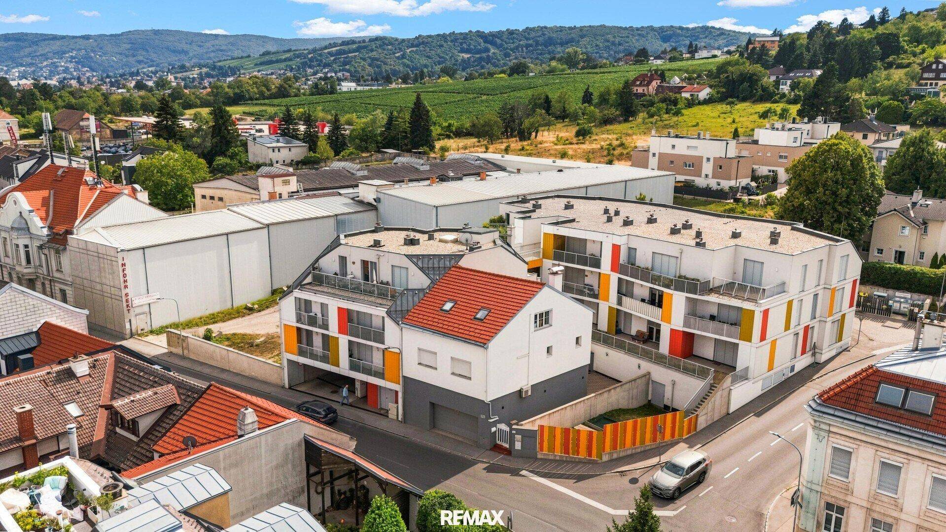 Weitläufige Luftaufnahme einer Wohnsiedlung mit modernen Gebäuden und grüner Hügellandschaft im Hintergrund.