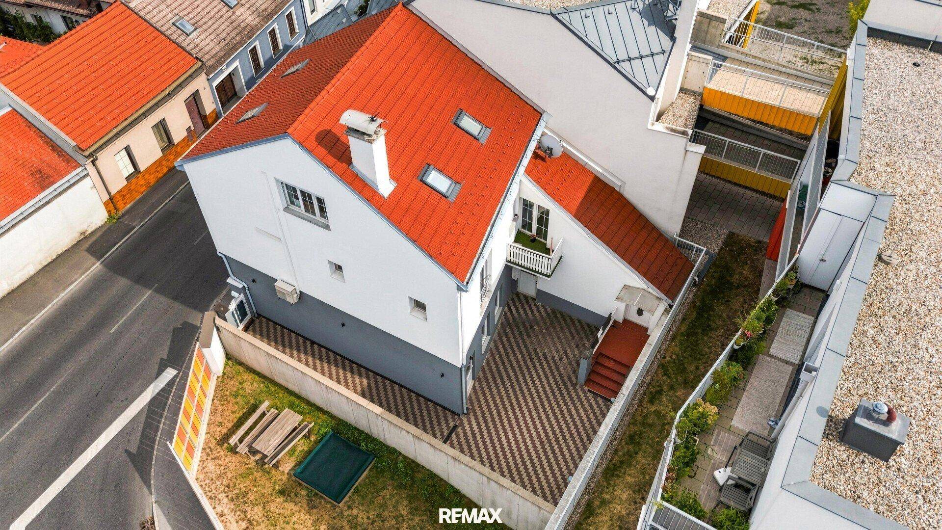 Luftaufnahme eines Wohnhauses mit rotem Satteldach, gepflastertem Hof und kleinem Balkon.