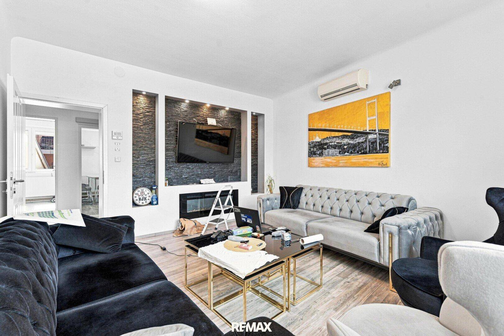 Modernes Wohnzimmer mit zwei Sofas, Holzboden und einem Wandelement mit Fernseher und Kamin.