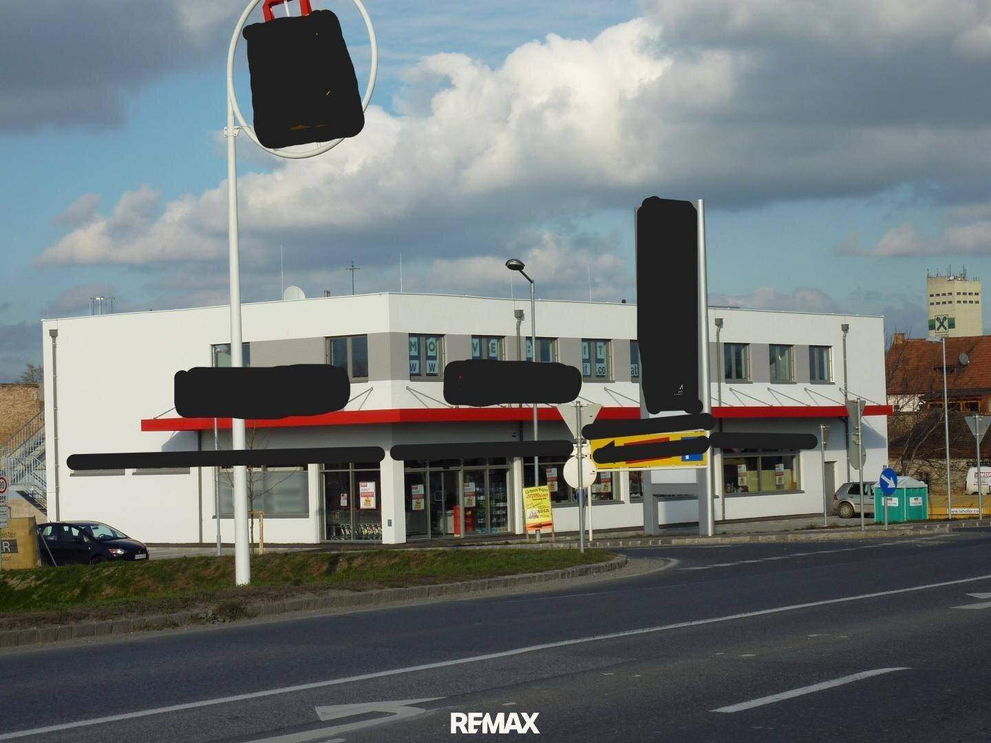 Frontansicht des Geschäftsgebäudes von der gegenüberliegenden Straßenseite, mit Werbetafeln und Parkplätzen.