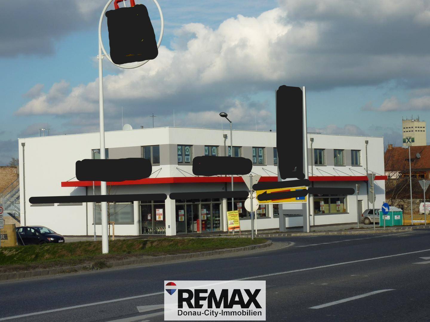 Geschäftsgebäude von der Straße aus gesehen mit großen Fenstern, rotem Vordach und Werbeflächen.