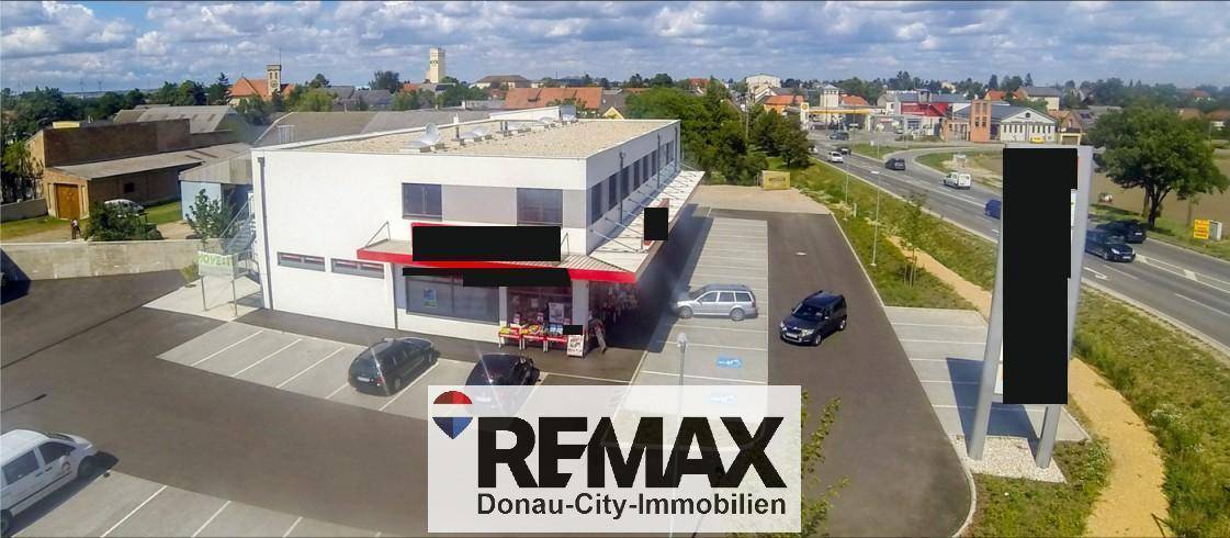 Weitläufige Ansicht des Geschäftsgebäudes mit umliegenden Parkplätzen und der angrenzenden Straße unter blauem Himmel.