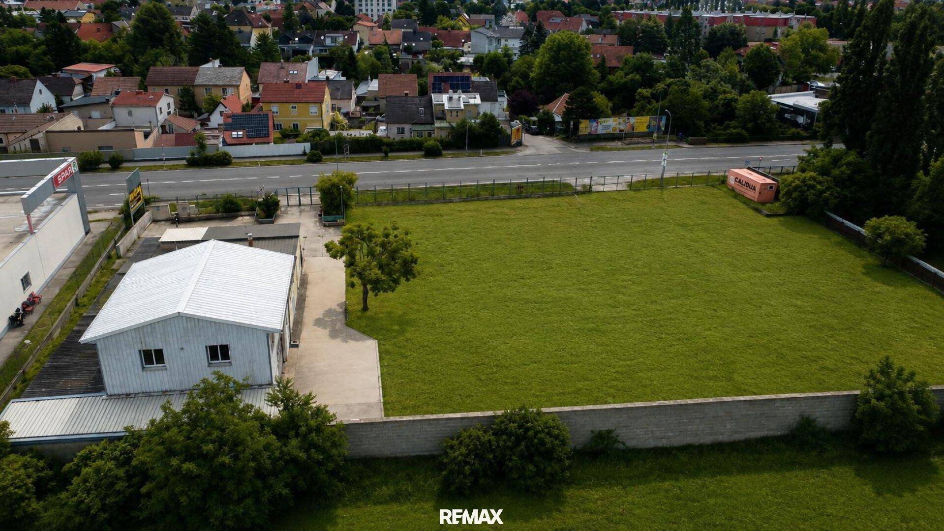 Luftaufnahme eines weitläufigen, grünen Grundstücks mit einem Gebäude, einer Straße und umliegenden Wohnhäusern.