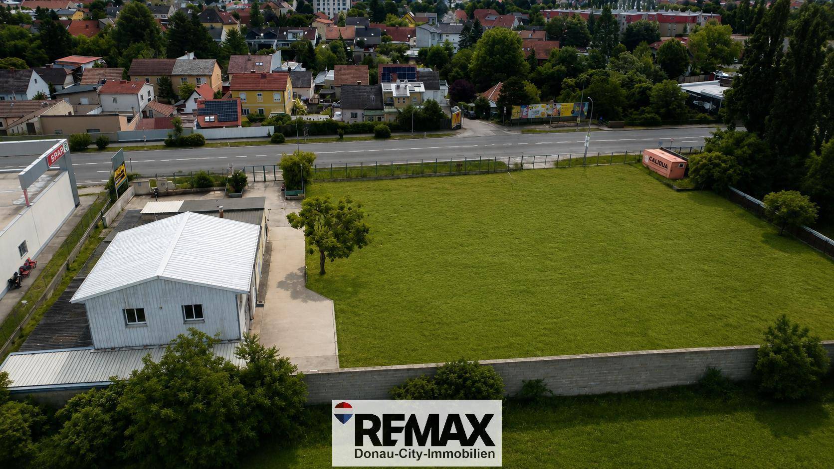 Nahaufnahme aus der Luft eines Gebäudes auf einem großen grünen Grundstück mit gepflasterter Fläche und Straße.