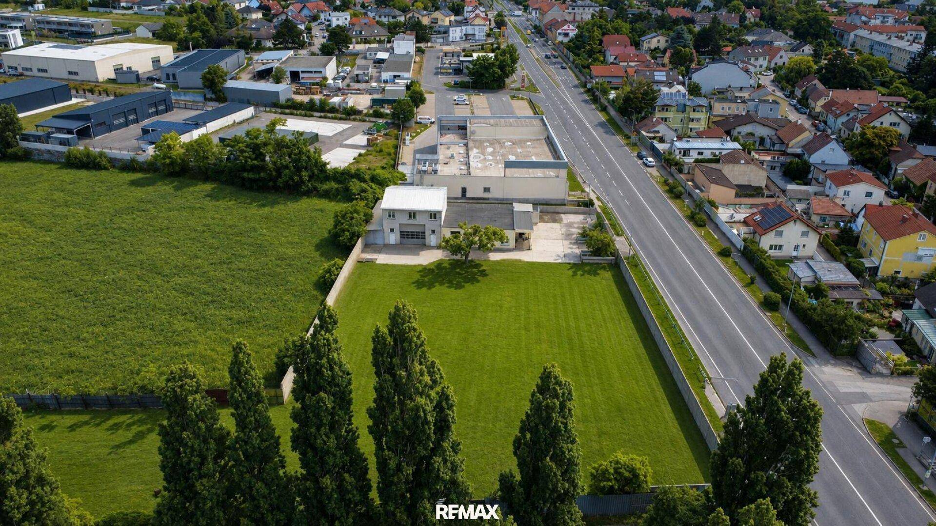 Weitläufige Luftaufnahme eines Grundstücks mit angrenzender Straße und einer Mischung aus Wohn- und Gewerbegebäuden.