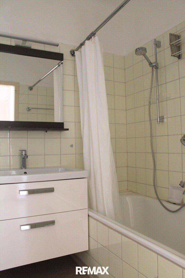 Badezimmer mit Badewanne, Duschvorhang, Einzelwaschbecken und hellbeigen Wandfliesen.