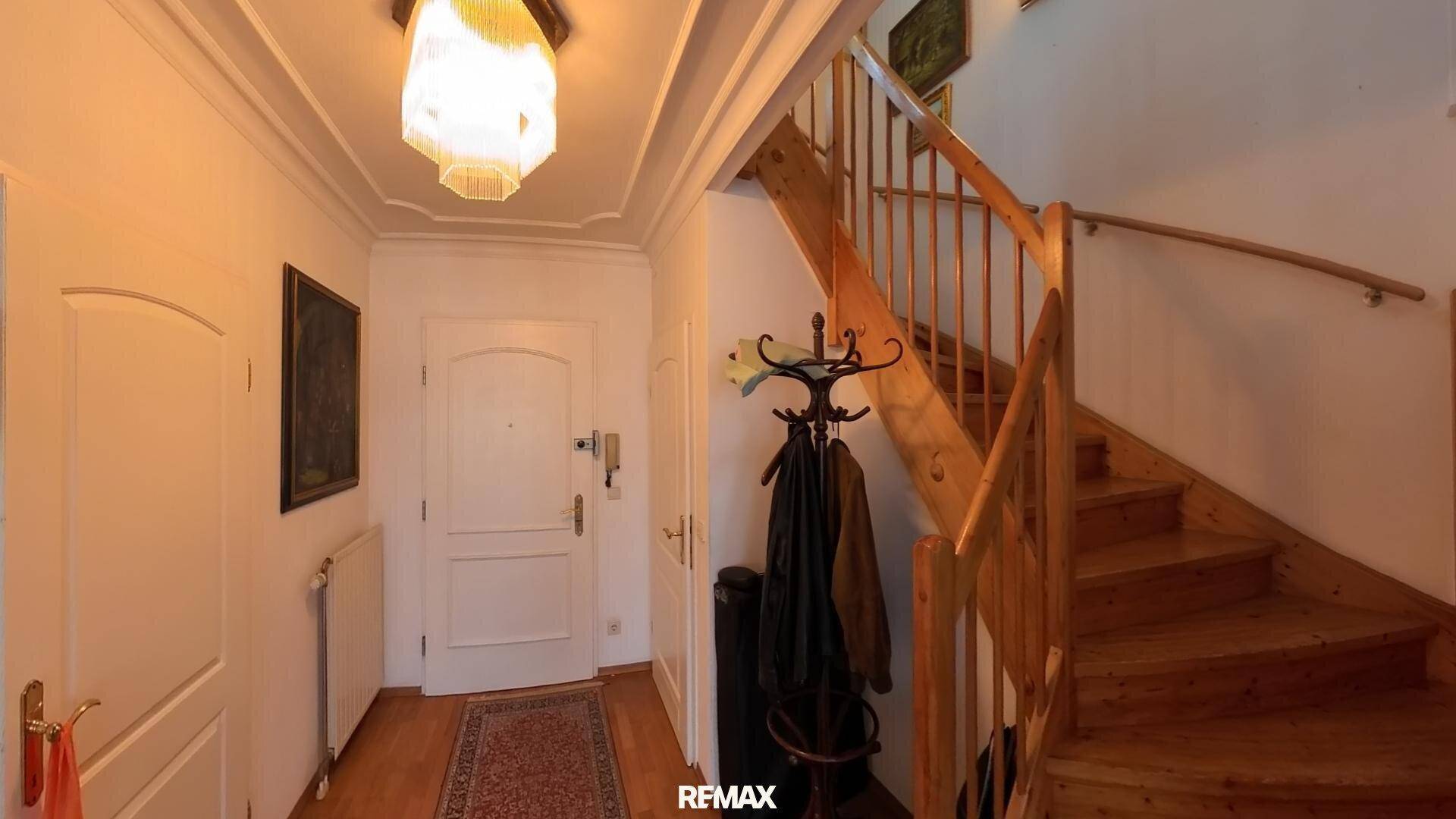 Heller Eingangsbereich mit Holztreppe und Garderobe, der zu den oberen Etagen führt.
