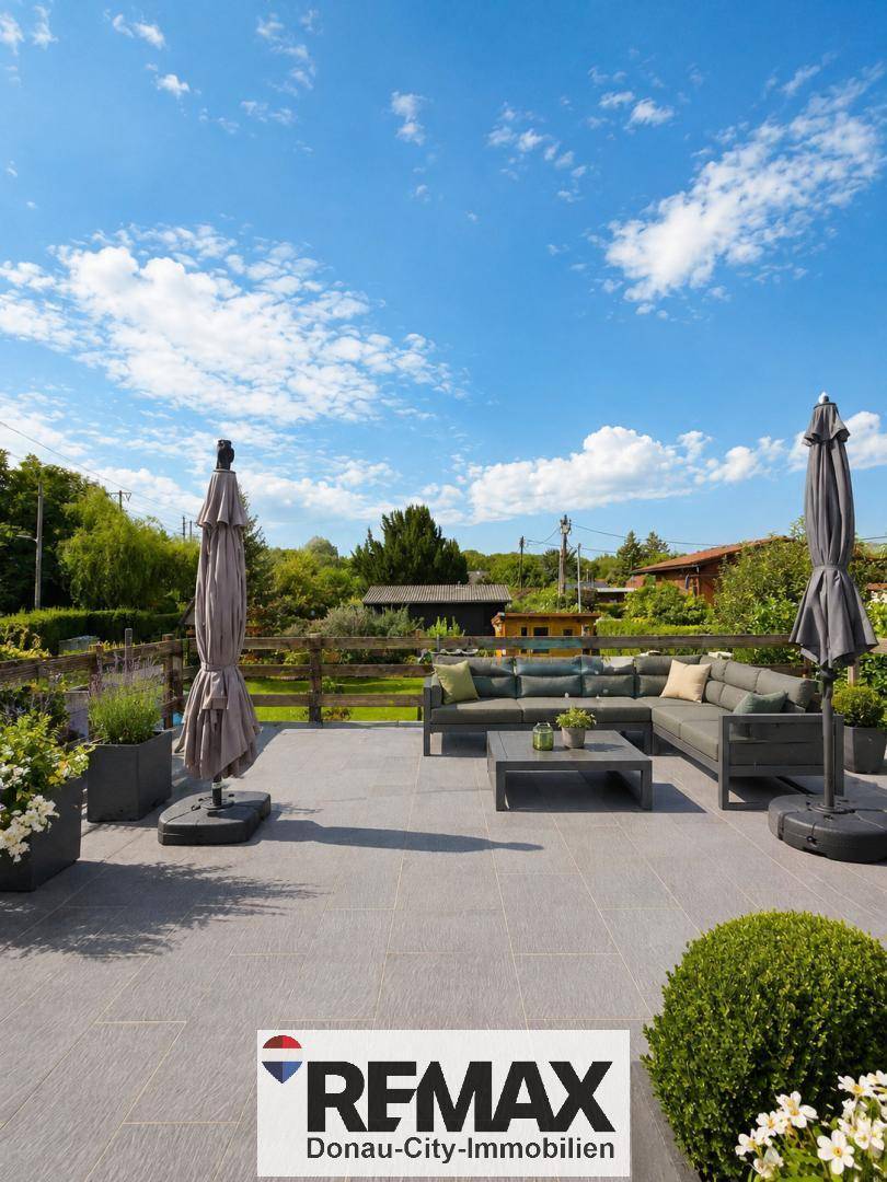 Geräumige Terrasse mit modernen Lounge-Möbeln, Esstisch und Sonnenschirmen auf Fliesenboden.