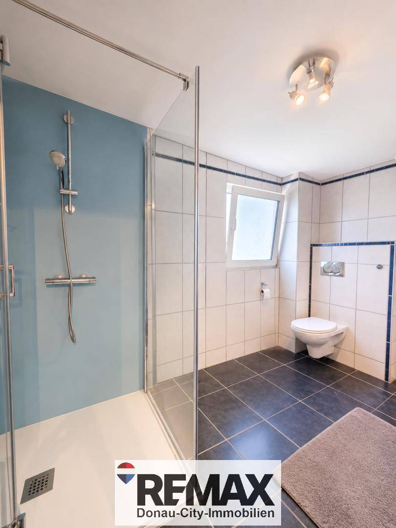 Modernes Badezimmer mit ebenerdiger Dusche, Wand-WC und blauen sowie weißen Fliesen.