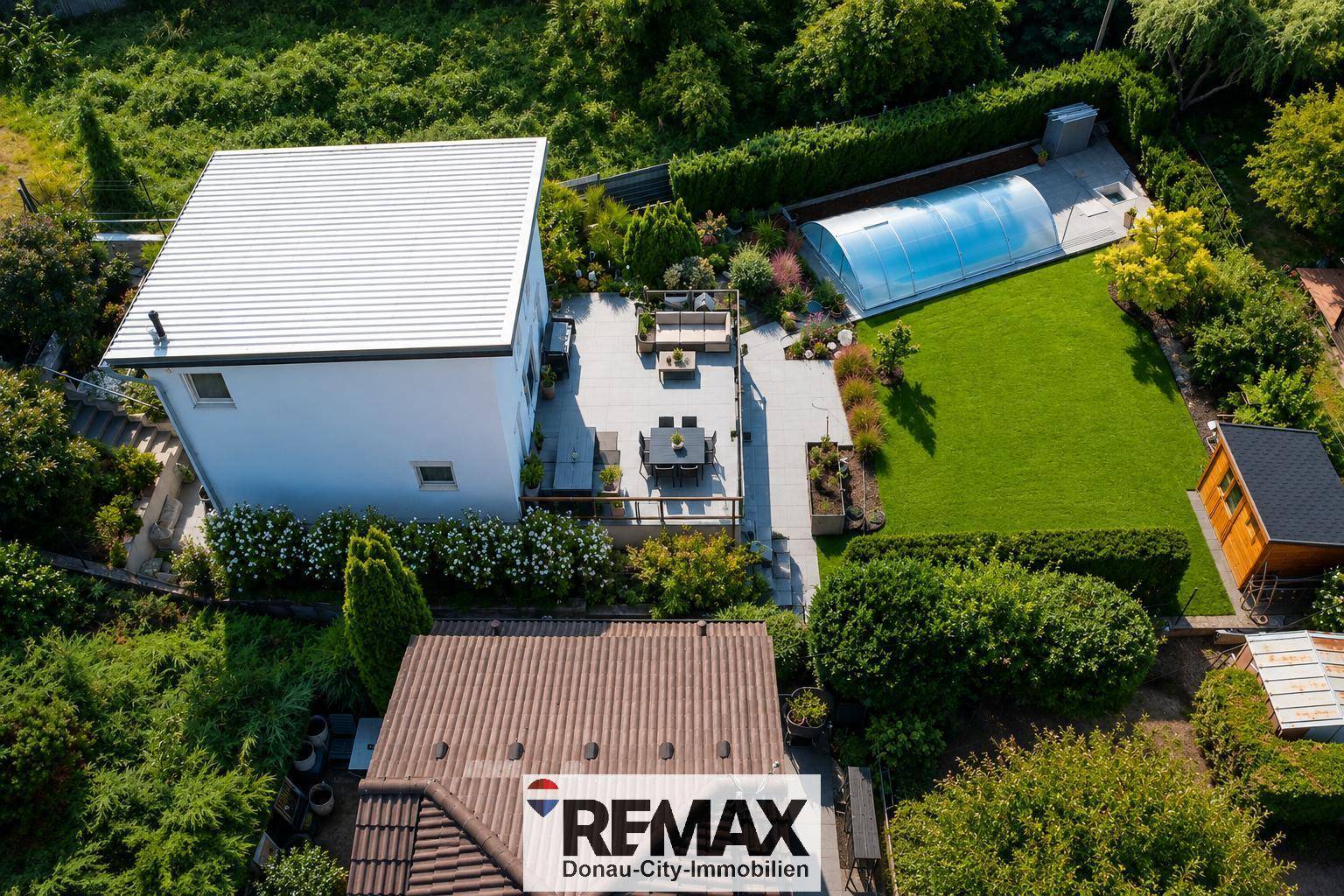 Vogelperspektive des Anwesens mit Haus, weitläufigen Terrassen, Garten und überdachtem Pool.