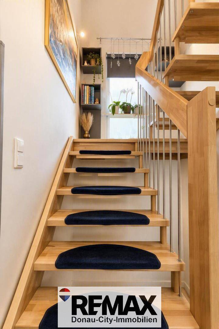 Helle Holztreppe mit blauen Teppichläufern und modernem Geländer führt in die obere Etage.