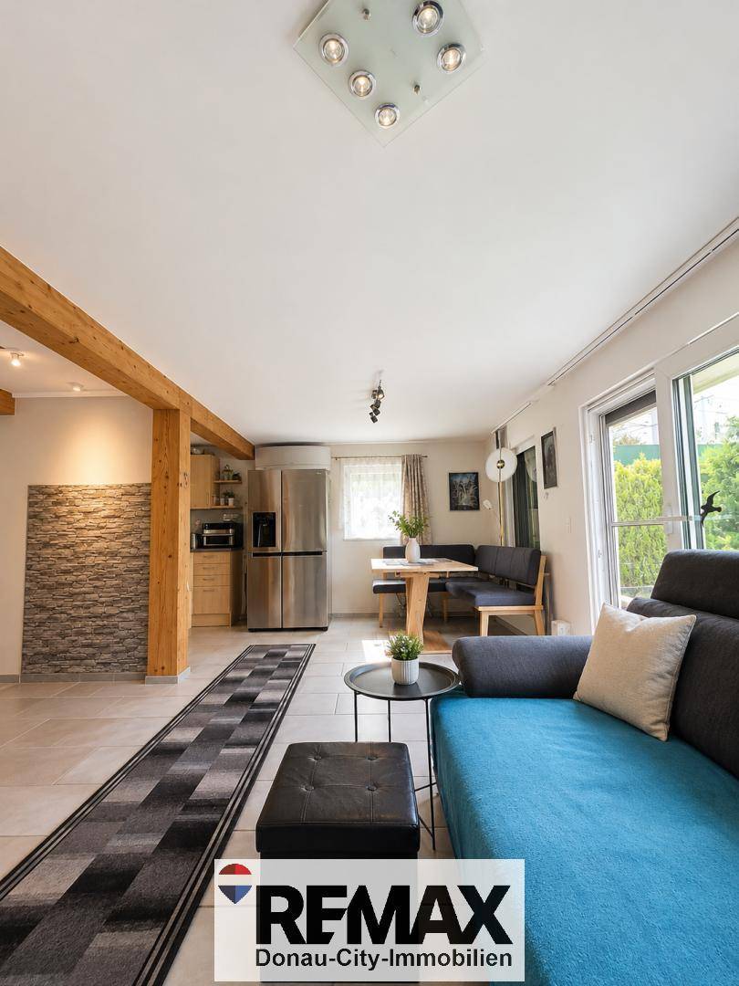 Offener Wohn- und Essbereich mit Sofa, Esstisch und integrierter Küche im Hintergrund.