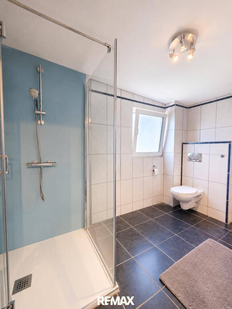 Modernes Badezimmer mit ebenerdiger Dusche, WC und Fliesenboden.