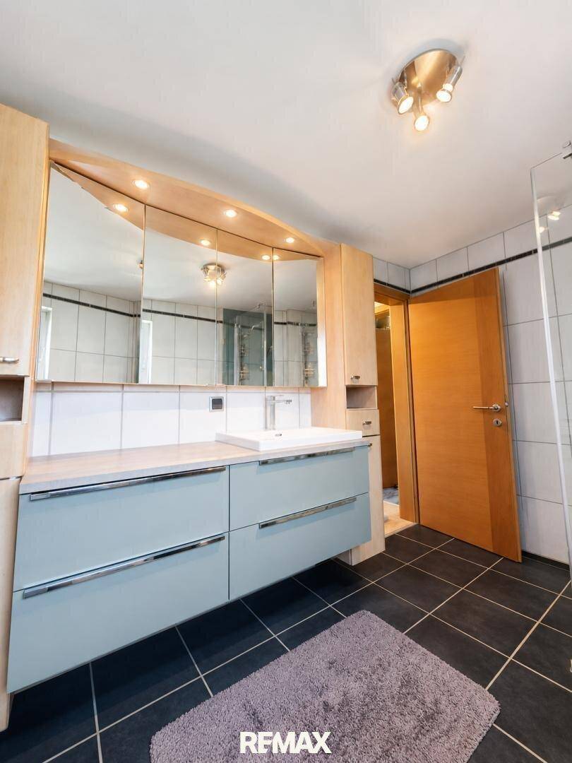 Badezimmer mit modernem Waschtisch, Spiegelschrank und dunklen Bodenfliesen.