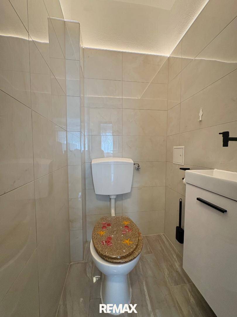 Separates WC mit hellen Fliesen, wandhängendem Waschbecken und modernem Design.