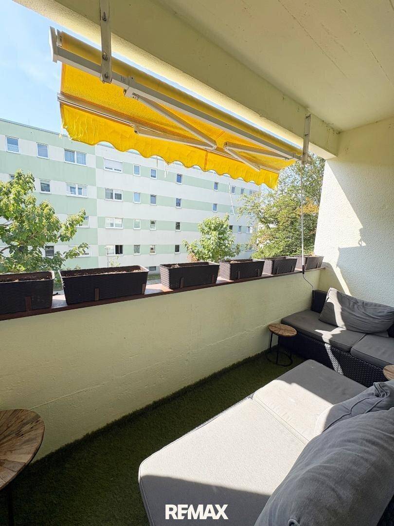 Gemütlicher Balkon mit Kunstrasen, Loungemöbeln und gelber Markise, ideal zum Entspannen.