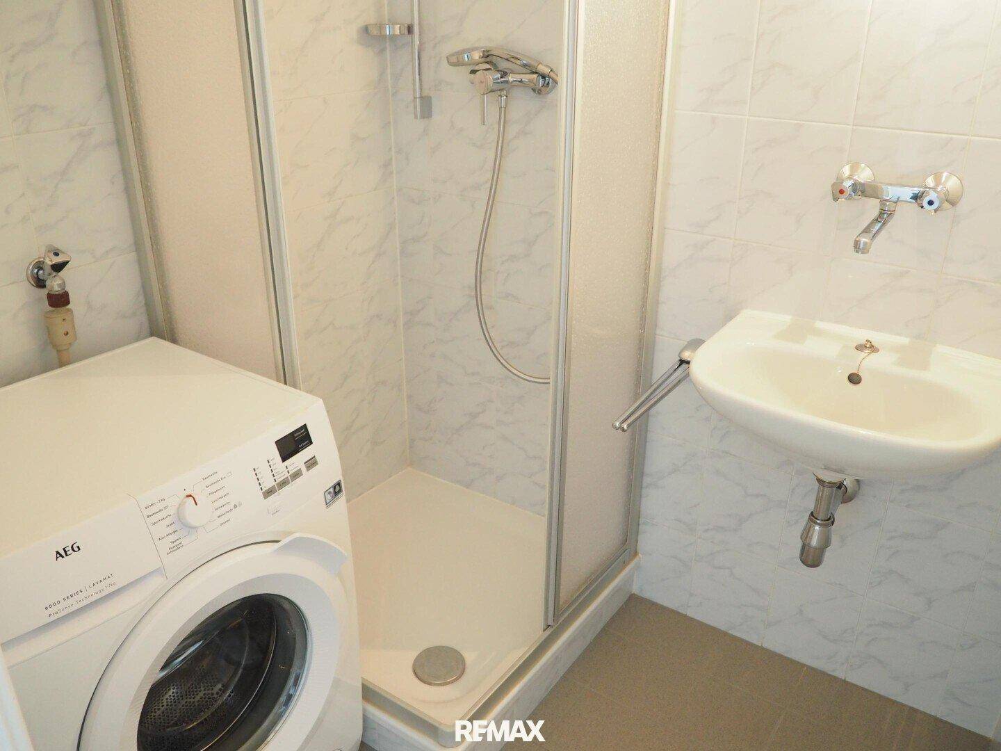 Funktionales Badezimmer mit Dusche, Waschbecken und Waschmaschine, hell gefliest.