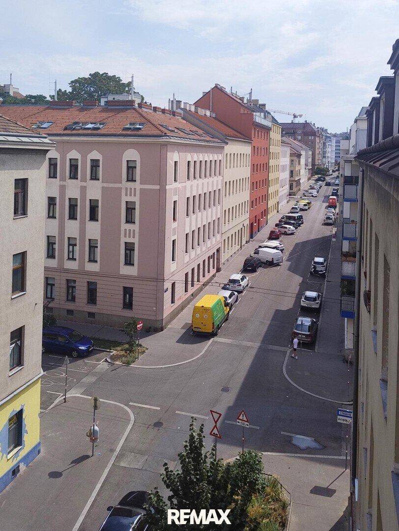 Blick von oben auf eine belebte Stadtstraße mit parkenden Autos und Gebäuden.