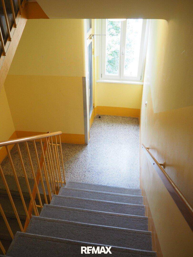 Treppenhaus mit Terrazzoboden und Fenster, das Tageslicht hereinlässt.