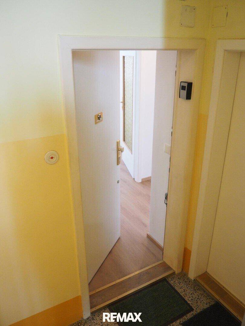 Eingangsbereich mit offener Tür zu einer Wohnung, heller Terrazzoboden.