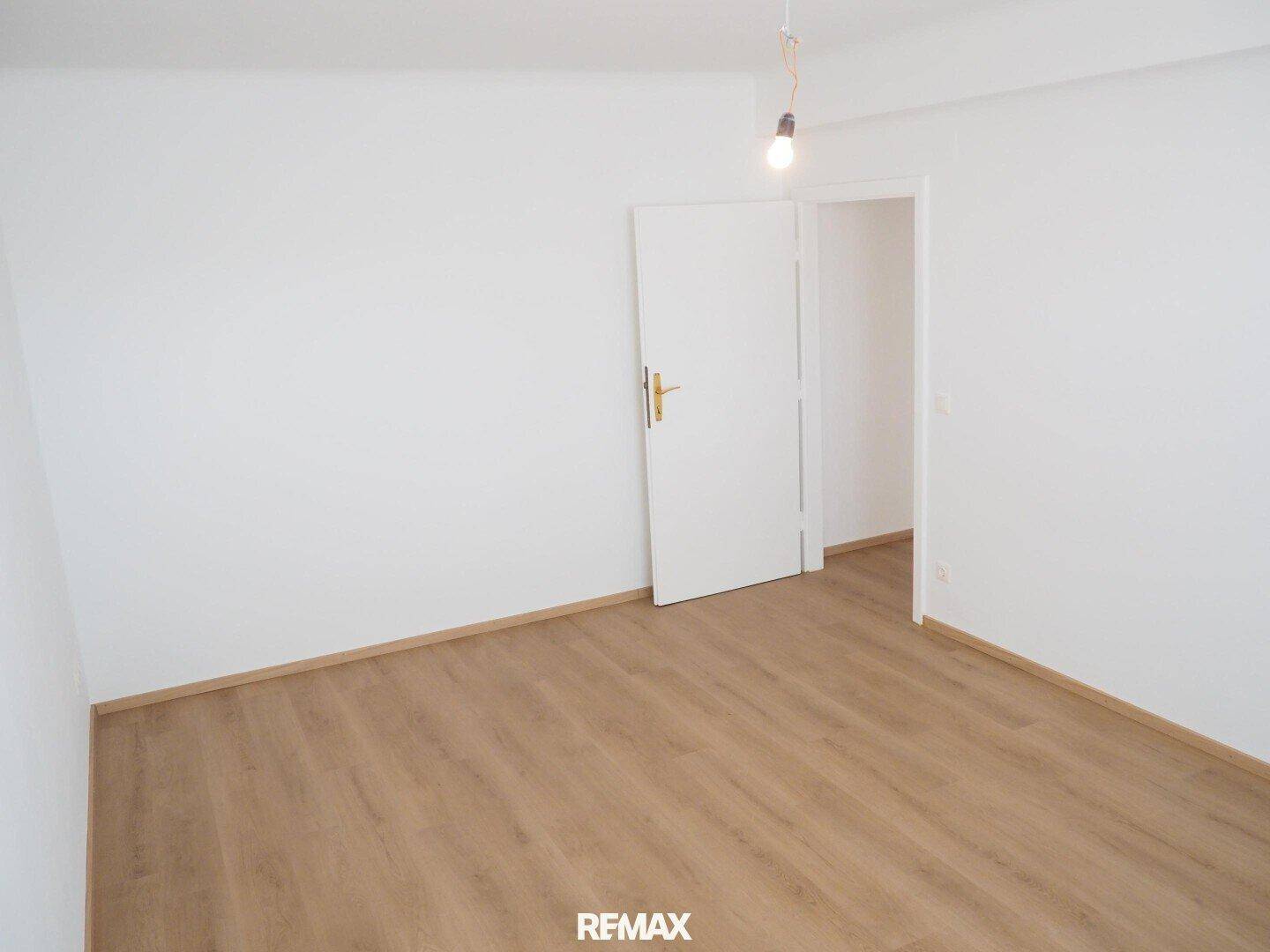 Leeres Zimmer mit Laminatboden und weißer Tür, bereit für individuelle Gestaltung.