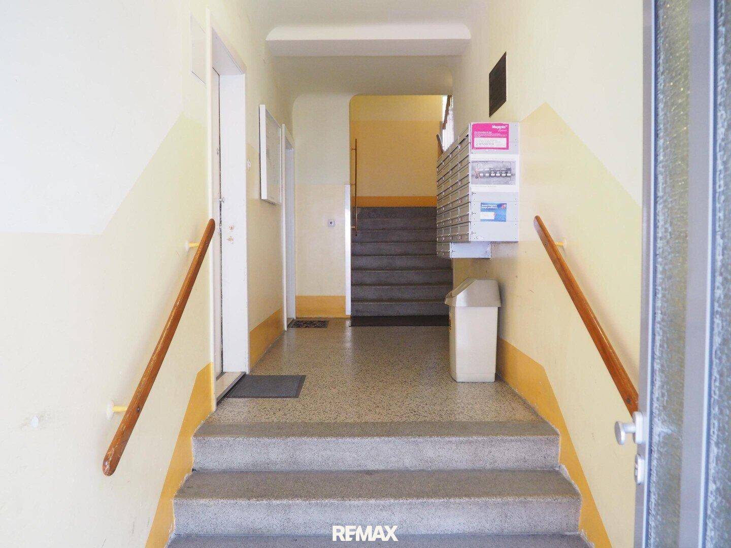 Eingangsbereich eines Mehrfamilienhauses mit Treppe und Briefkästen.