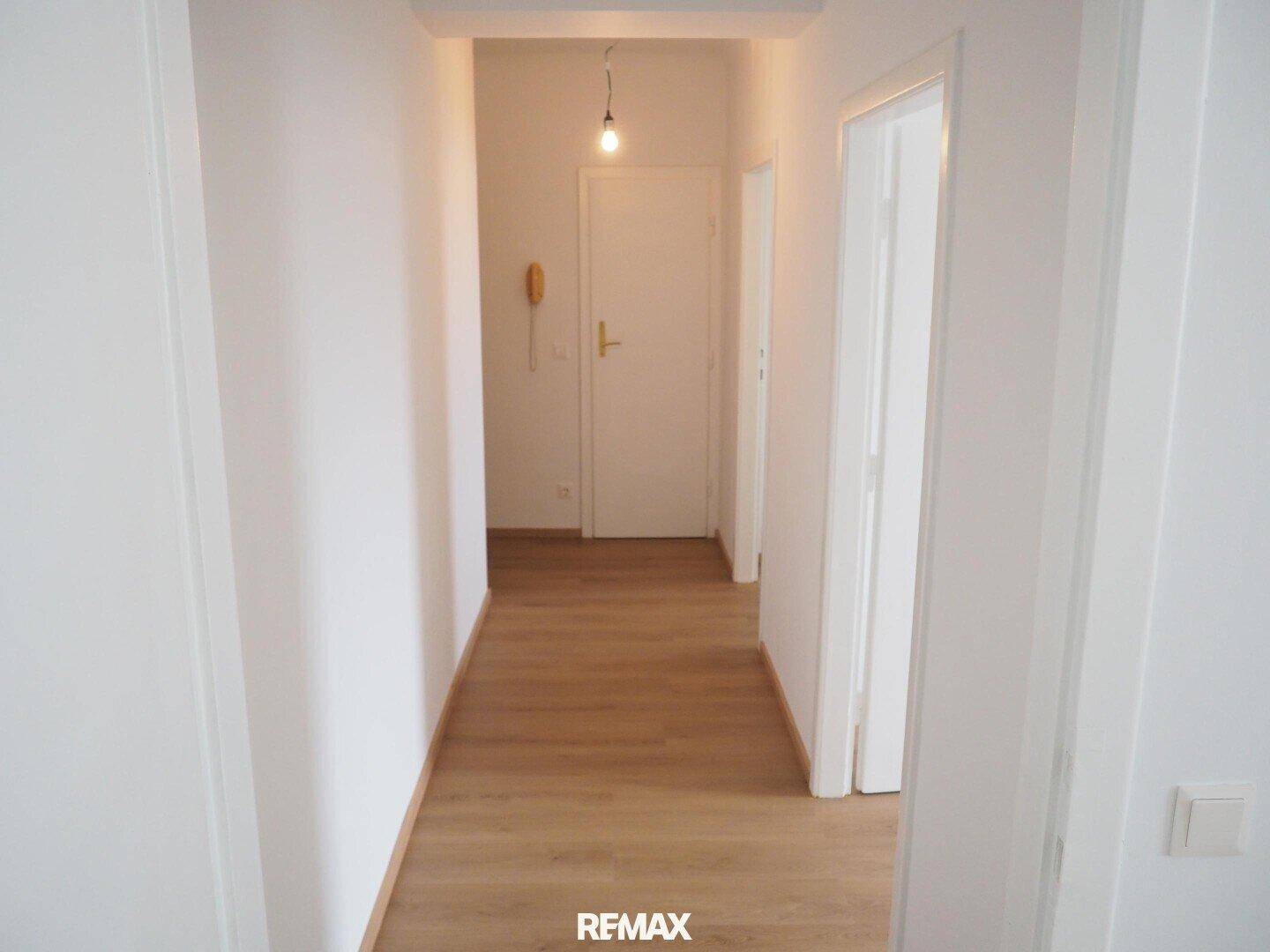 Heller Flur mit Laminatboden und Eingangstür, ausgestattet mit Gegensprechanlage.