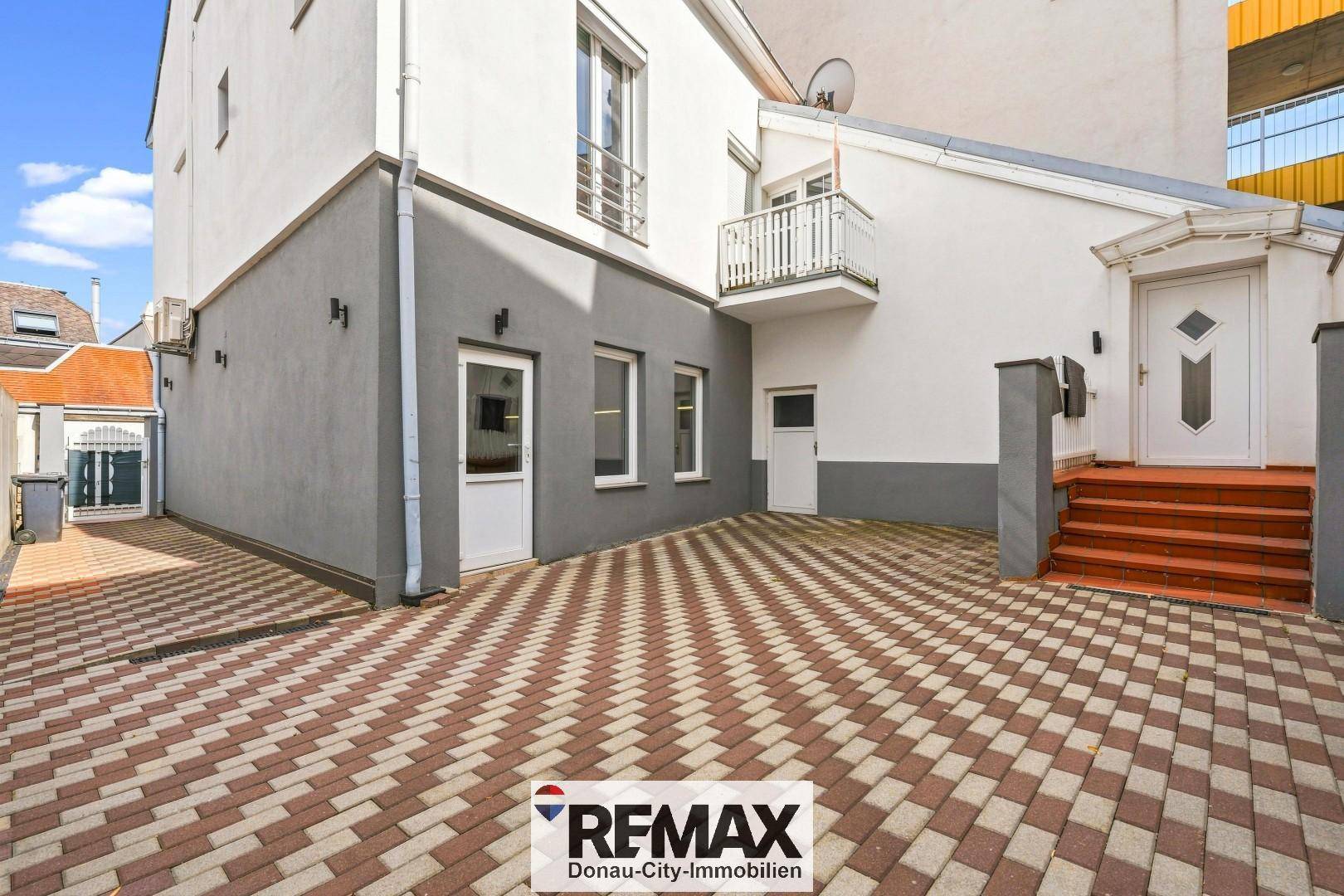 Rückseite des Gebäudes mit gepflastertem Hof, Außentreppe und kleinem Balkon.
