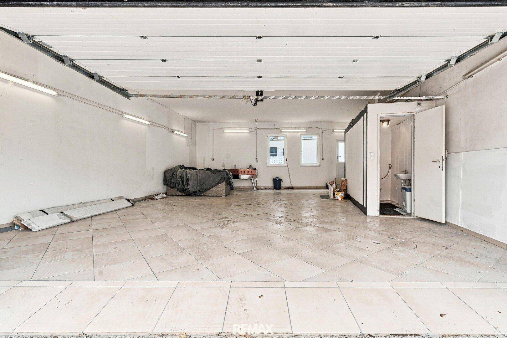 Geräumige Garage mit Fliesenboden, Beleuchtung und einem separaten WC-Bereich.