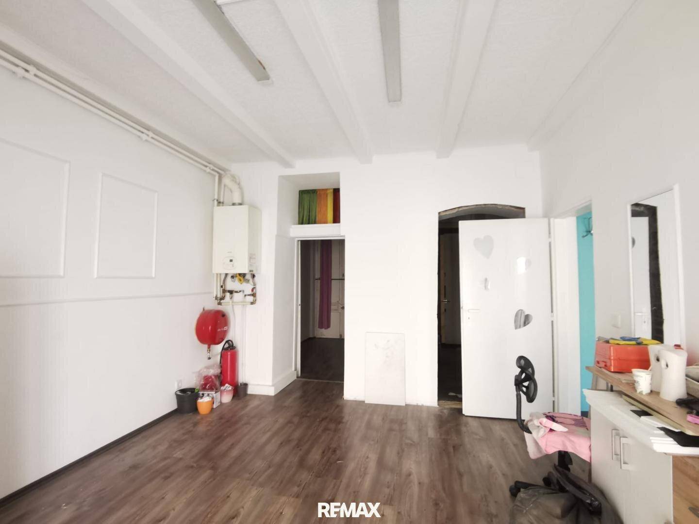 Heller Gewerberaum mit sichtbaren Deckenbalken, Laminatboden und einem Warmwasserbereiter an der Wand.