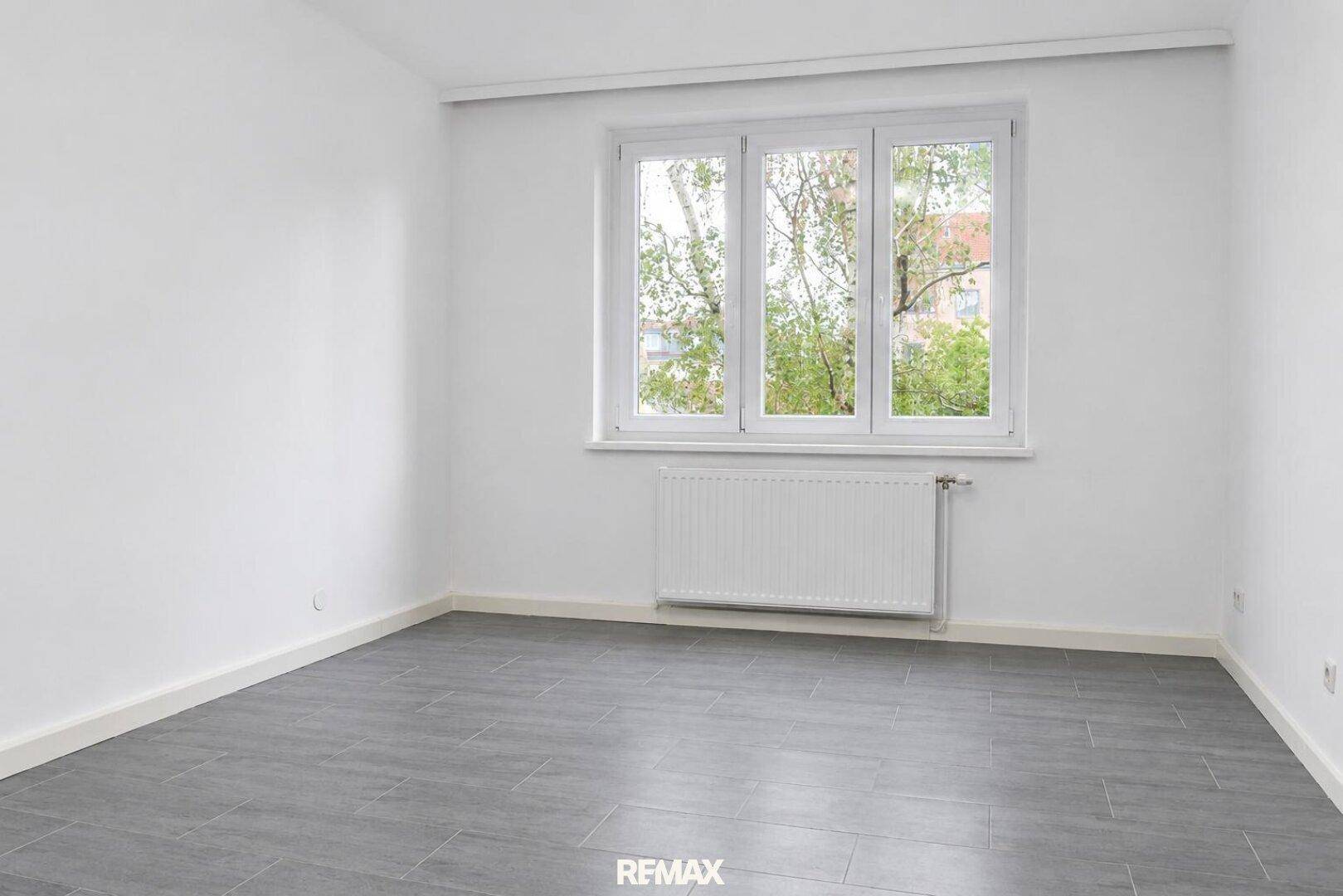 Geräumiges, leeres Schlafzimmer mit großem Fenster und viel Tageslicht.