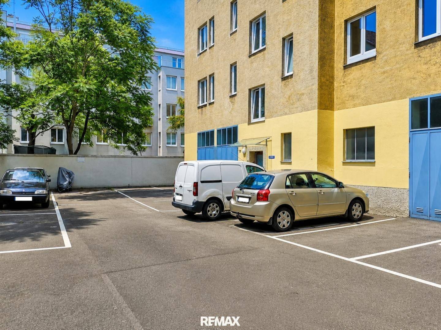 Außenparkplatz mit mehreren Fahrzeugen neben einem Wohngebäude unter blauem Himmel.