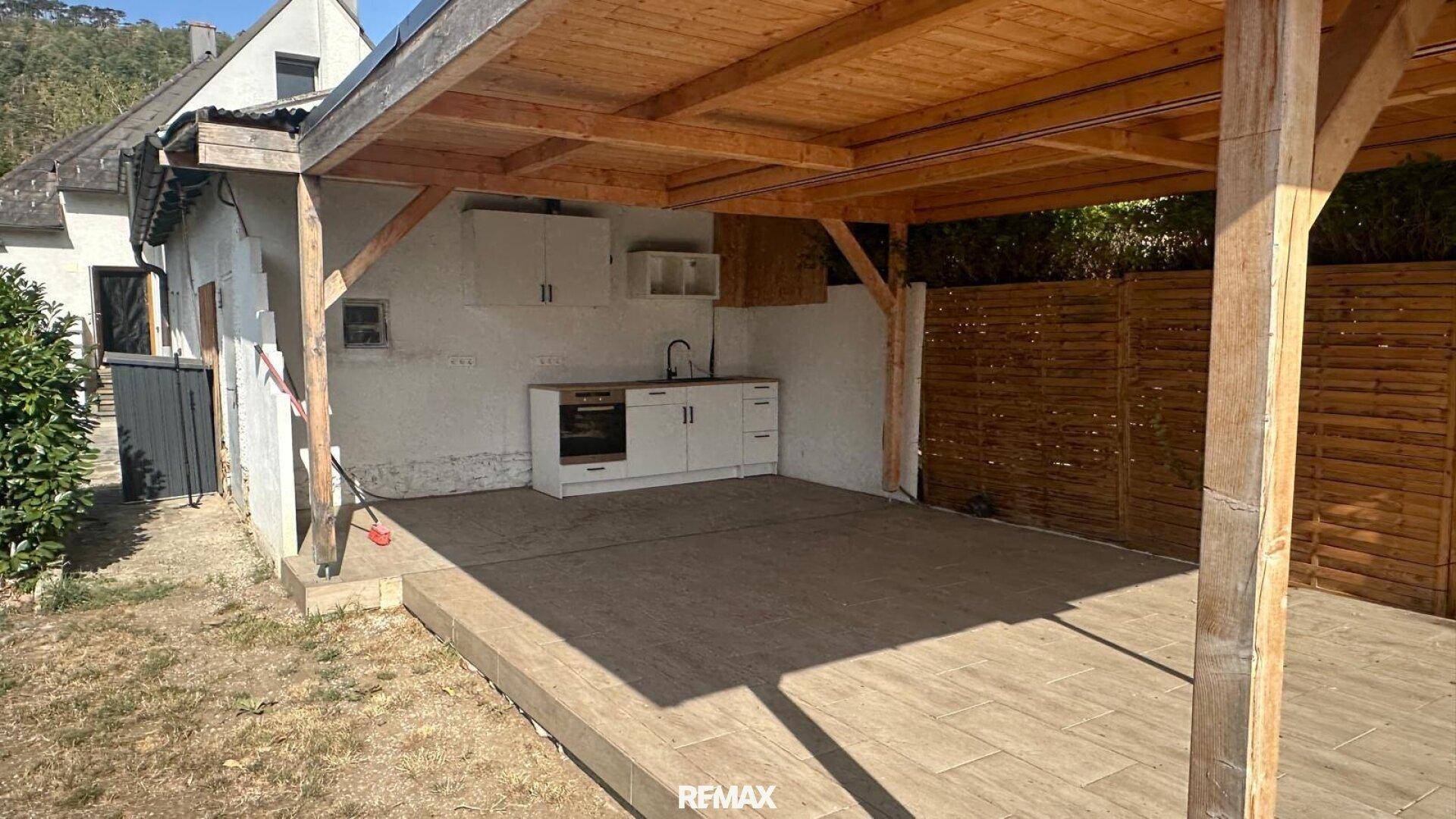 Überdachte Terrasse mit Außenküche, Holzverkleidung und Fliesenboden.
