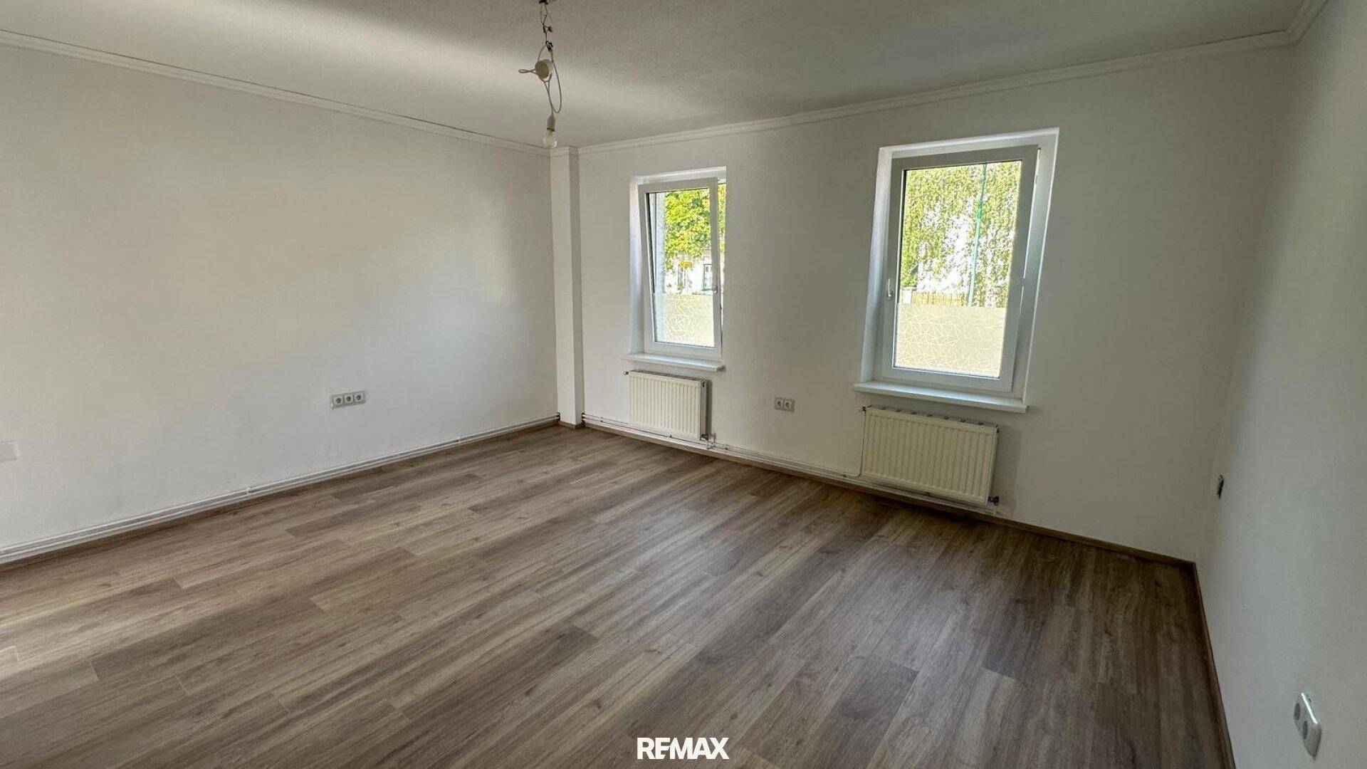 Geräumiger, heller Raum mit Laminatboden und zwei Fenstern, bereit zur individuellen Gestaltung.