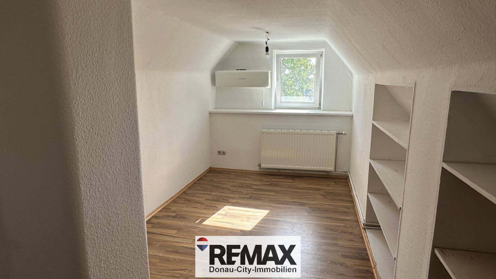 Helles Zimmer mit Dachschräge, Laminatboden, eingebauten Regalen und Klimaanlage.