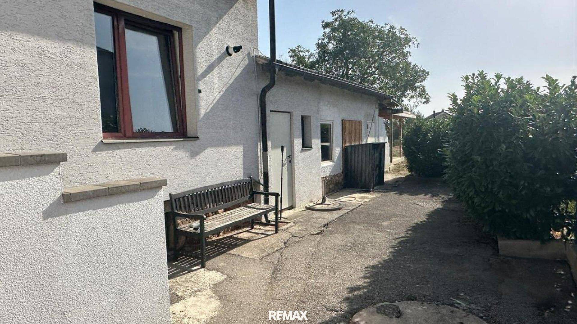 Seitenansicht des Hauses mit einem kleinen Anbau und einem gepflasterten Weg.